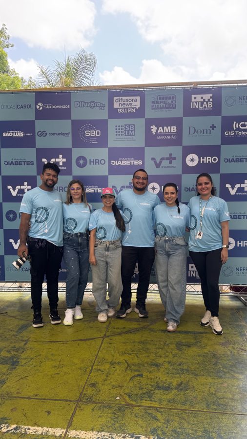 Equipe da Abacaxi em frente ao painel de patrocinadores de um evento de saúde